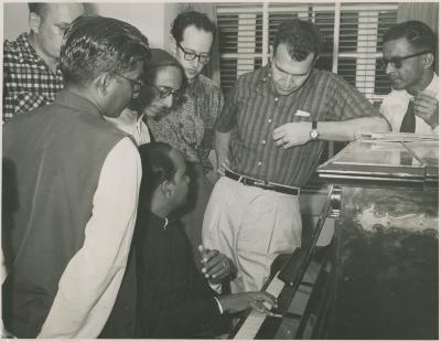 Dave Brubeck leaning on piano played by an unidentified Indian musician, Paul Desmond, unidentified Indian men (Mumbai, India)