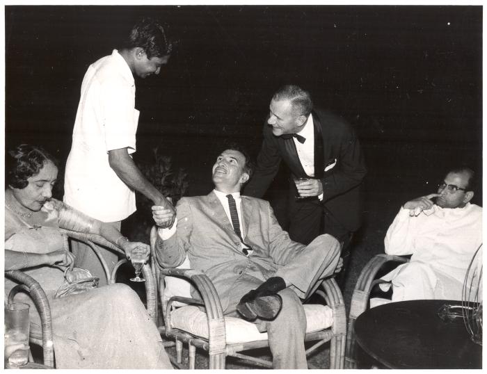 Dave Brubeck meeting unidentified Indian musician at a reception; unidentified woman to the left, to the right John Wiggin leans over Dave Brubeck, S. Balachander seated to the right (India)