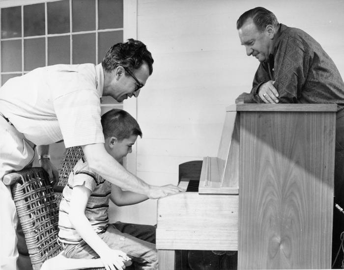 Dave Brubeck and Chris Brubeck at the piano, Walter Cronkite looking on during filming of an episode of the CBS television show "The 20th Century" at Dave Brubeck's home (Wilton, Connecticut)